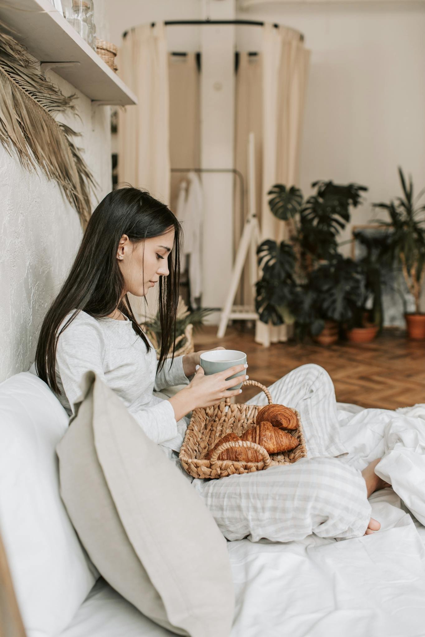 Woman enjoying a cozy morning with breakfast in bed, featuring croissants and coffee.